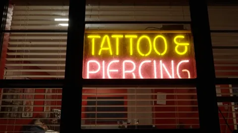 Tattoo shop promo video in St. Louis: neon Tattoo and Piercing sign glowing in a shop window at night