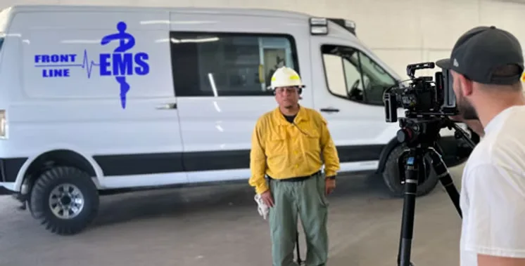 Medical video production on location: Front Line EMS crew member in a yellow shirt and hard hat filmed by MEM Films beside a Front Line EMS van