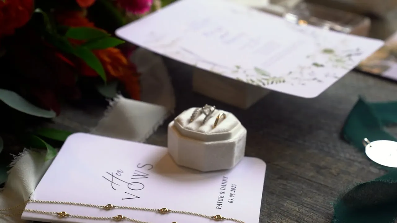 Danny and Paige wedding film: ring box and handwritten vows book beside the invitation suite